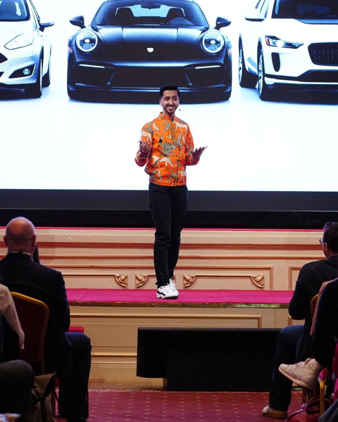 Asad Dhunna speaking on stage to a seated audience